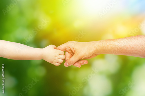 young child holds the hand of his father on green background © fidaolga