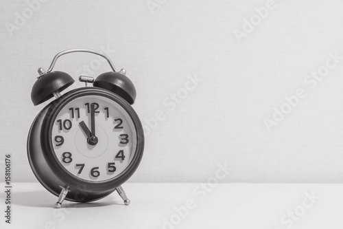 Closeup alarm clock for decorate in 11 o'clock on white wood desk and cream wallpaper textured background in black and white tone with copy space