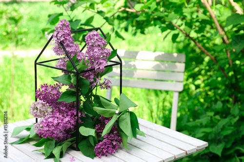 Cage with beautiful lilac flowers on table in garden