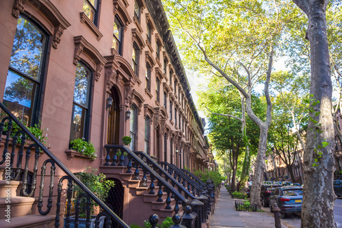 Scenic view of a classic Brooklyn brownstone block with a long facade and ornate stoop balustrades on a summer day in New York City