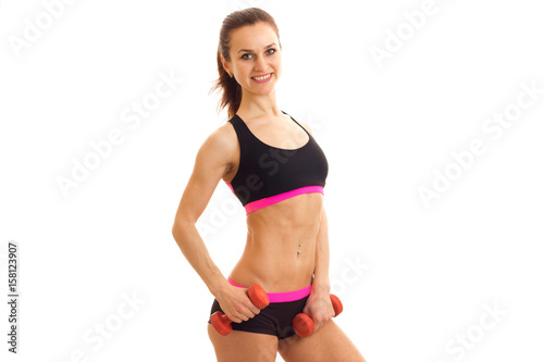 a svelte young fitness girl with beautiful waist smiling looks at the camera and holding a dumbbell