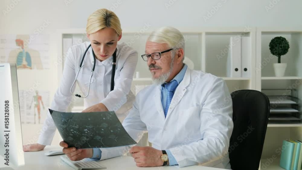 Midle aded caucasian senior doctor man and young caucasian female doctor looking x-ray image and talking about it. Indoor.