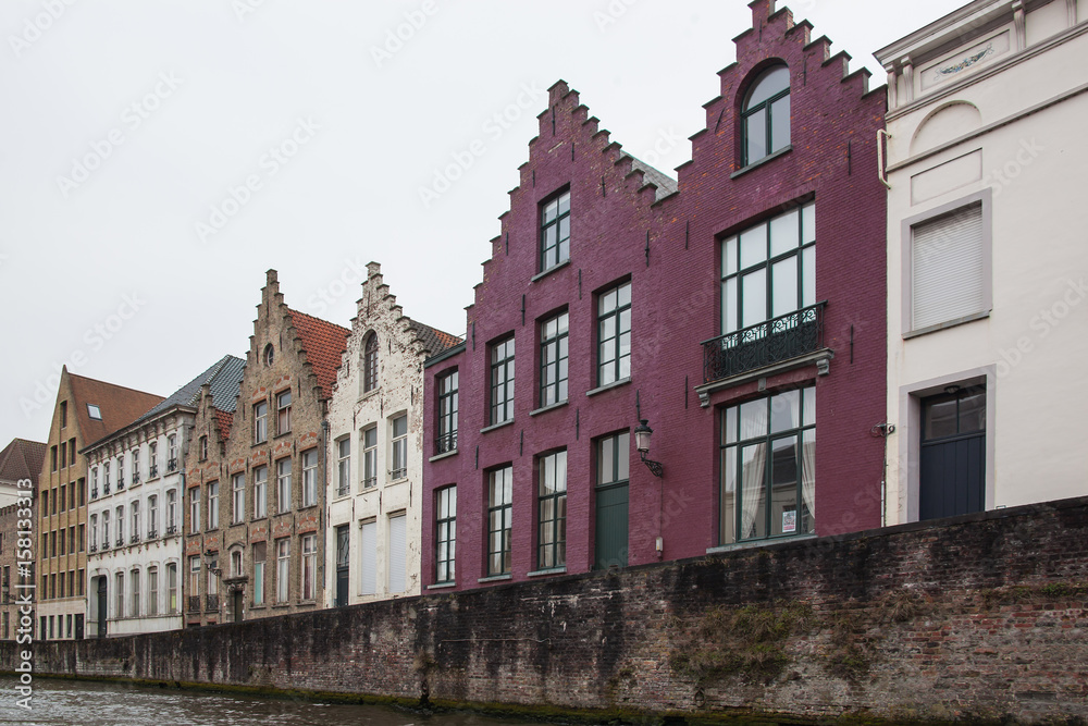 View of the picturesque facades of historic buildings from canal in the  tourist center of Bruges (Brugge) on a cloudy day, Belgium