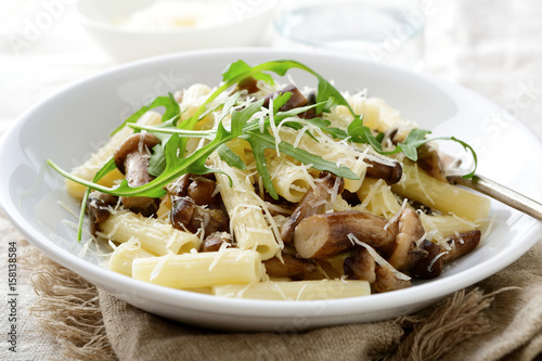 Italian traditional pasta with mushrooms and arugula in white bowl
