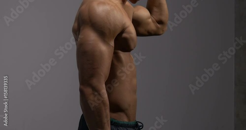 The muscular torso of a fitness model is filmed from profile. The model holds up his arm flexing his bicep and smiles at the end of the pose.