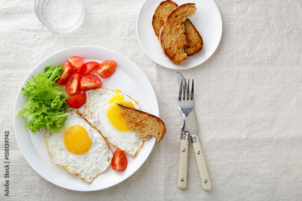 Fried Eggs with lettuce, tomato and bread on a linen tablecloth Fried Eggs with lettuce, tomato and bread on a linen tablecloth