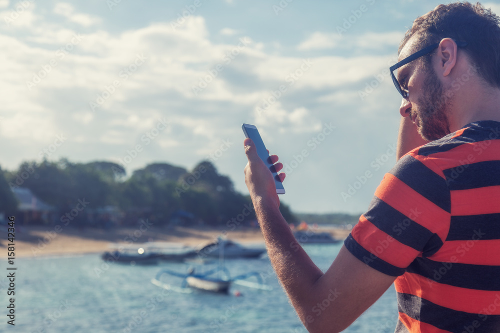 Young man using cellphone / smartphone near ocean.
