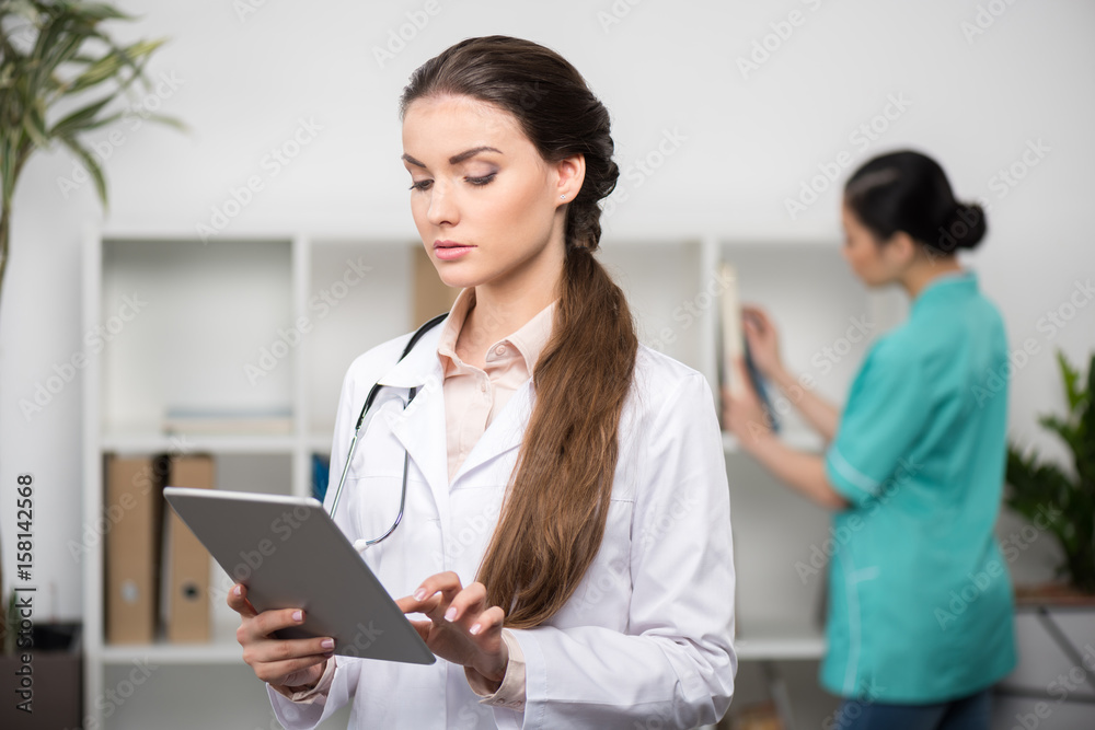 confident doctor wearing white coat and using digital tablet, internist standing behind in clinic confident doctor wearing white coat and using digital tablet, internist standing behind in clinic