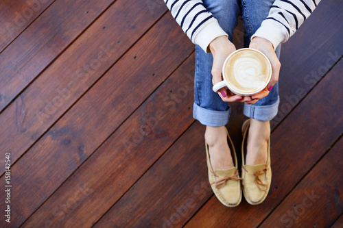 Woman holding in hands cup of coffee with milk sitting on the floor