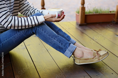 Woman holding in hands cup of coffee with milk on the floor