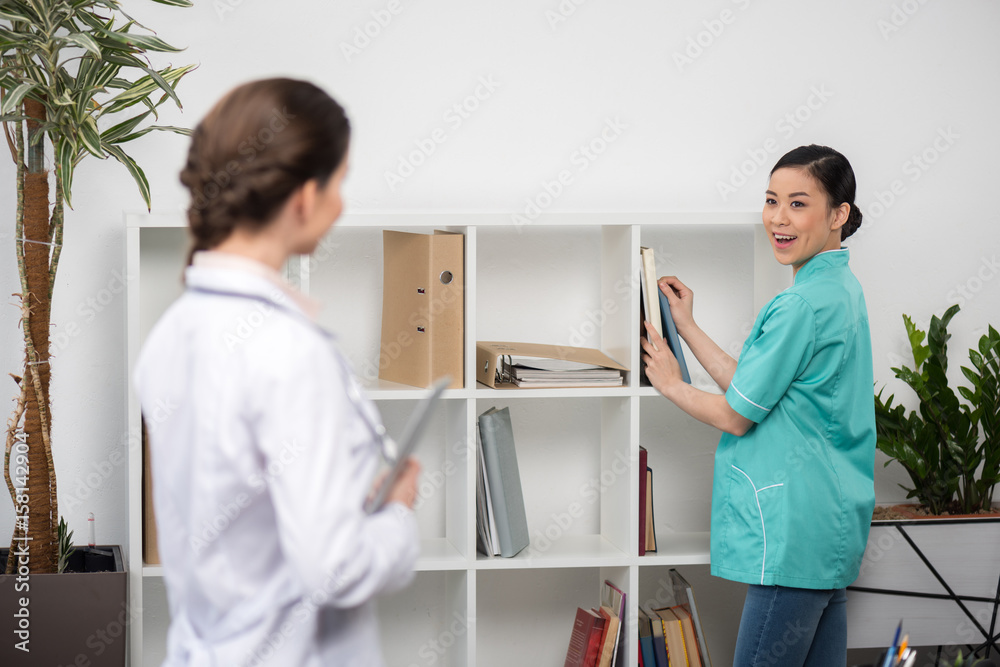 Fototapeta premium smiling internist talking with doctor in clinical office, focus on background
