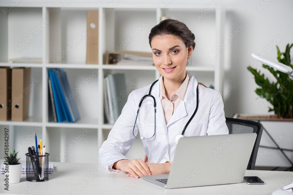 young caucasian doctor using laptop and looking at camera in clinic