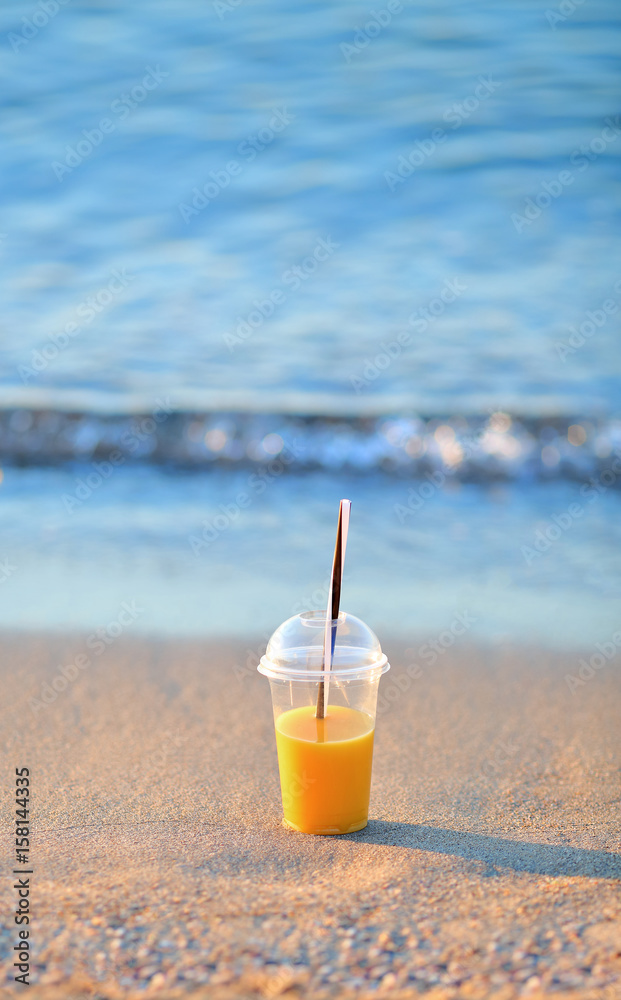 Orange juice in a disposable cup in the sand on the beach Orange juice in a disposable cup in the sand on the beach