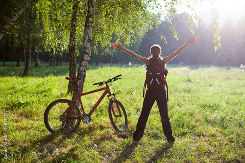 Excited girl cyclist standing in a spring park with hands outstretched