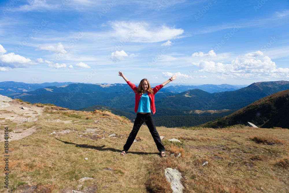 Tourist stretching out her arms while stands on peak of mountain