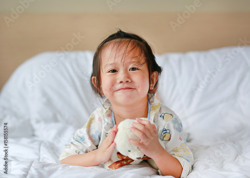 Cute little girl with teddy bear lying on bed.