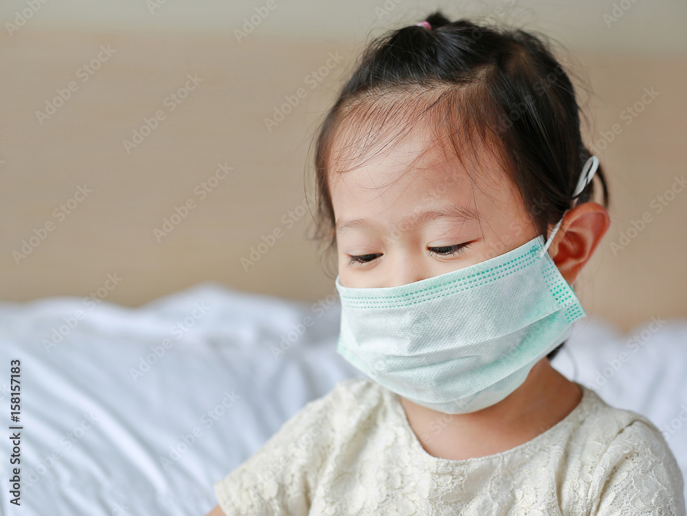 Little girl wearing a protective mask lying on the bed.