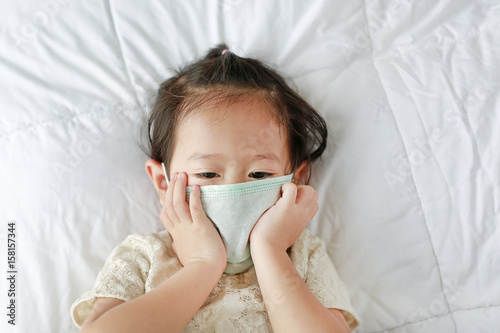 Little girl wearing a protective mask lying on the bed.