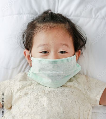 Little girl wearing a protective mask lying on the bed.