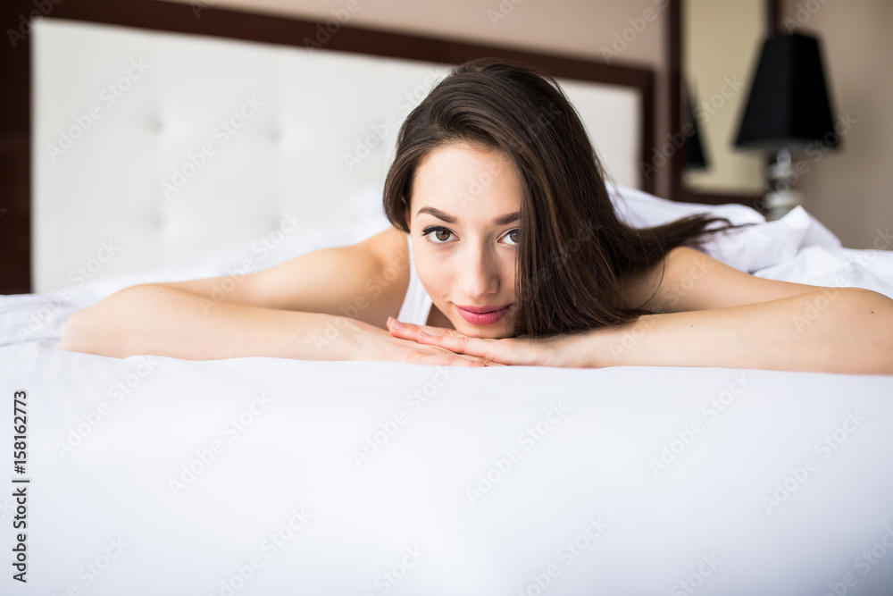 Woman lying at the end of the bed underneath the quilt and smiling, with her head resting upon her hand with the other in her hair. Woman lying at the end of the bed underneath the quilt and smiling, with her head resting upon her hand with the other in her hair.