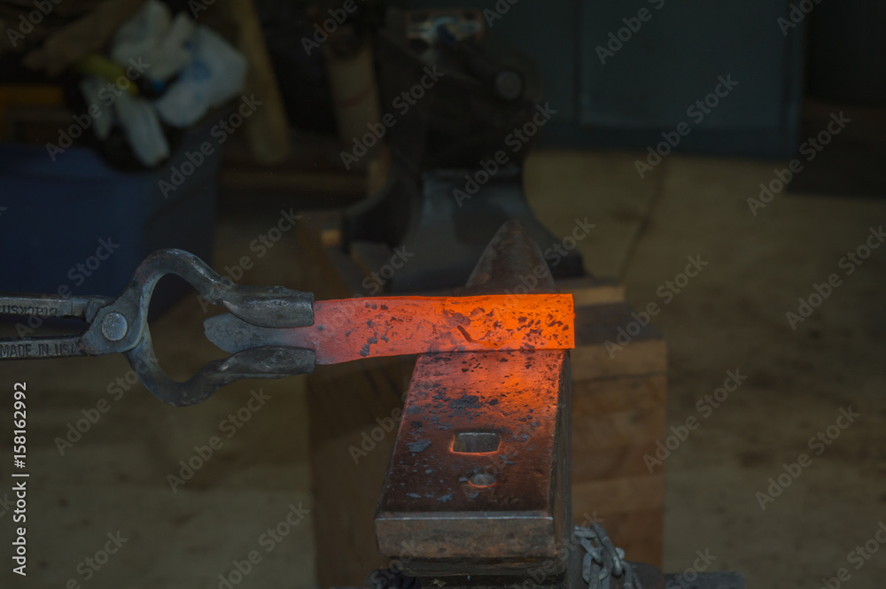 A billet of hot metal in the tongs of a bladesmith is about to be transformed into a useful knife