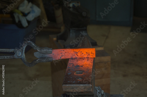 A billet of hot metal in the tongs of a bladesmith is about to be transformed into a useful knife photo