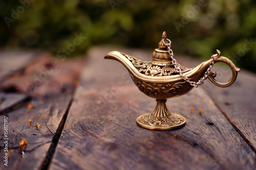 Close up of gold decorated magic lamp on wooden background.