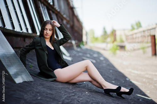 Sexy model girl wit long legs at black lingerie outfit body swimsuit combidress and jacket posed at the roof of abadoned industrial place with windows. © AS Photo Family