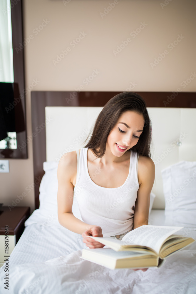 Woman lying in bed while reading a book at home Woman lying in bed while reading a book at home