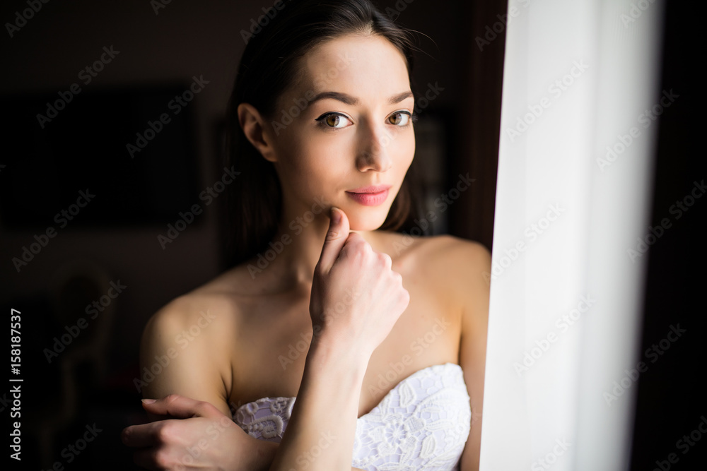 Beautiful woman near curtains of window and looking at the camera