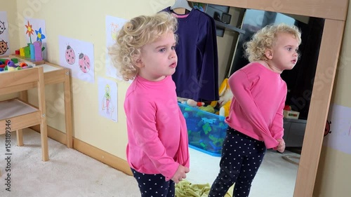 Adorable child unsuccessful try to undress clothes in front of mirror photo