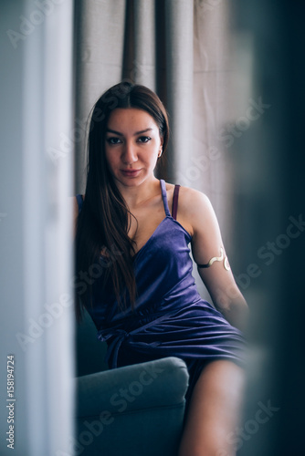 Sexy beautiful girl posing in a room with violet dress, photographed in a paparazzi styl,spied style with foreground unfocused