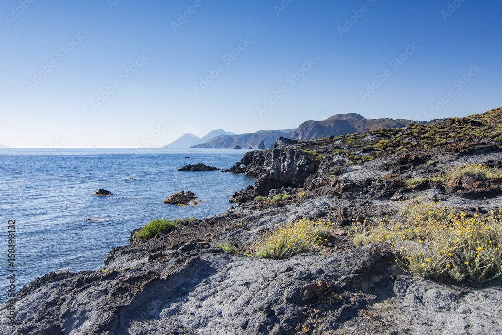 Scogliera di roccia vulcanica con vista su Lipari e Salina sullo sfondo, isola di Vulcano - arcipelago delle Isole Eolie IT