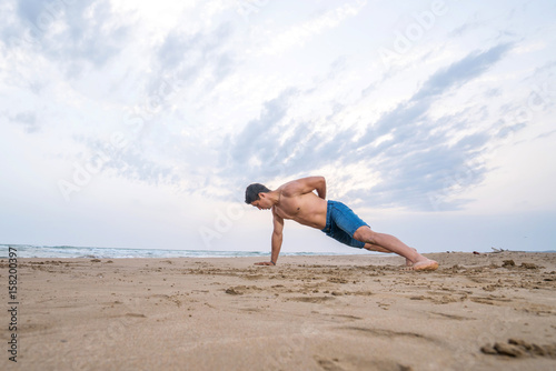 Fitness man doing push-up exercise on beach.