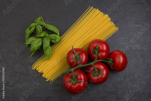 spaghetti basil and tomatoes on black slate stone background