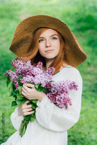 Redhead girl with a bouquet of lilacs in a spring garden