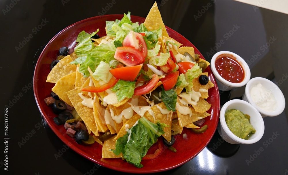 Nachos and three dips Nachos topped with tomatoes, green lettuce, olives and bacon bits in a round red plate, served with small bowls of ketchup, mayonnaise and avocado dip. Nachos and three dips Nachos topped with tomatoes, green lettuce, olives and bacon bits in a round red plate, served with small bowls of ketchup, mayonnaise and avocado dip.