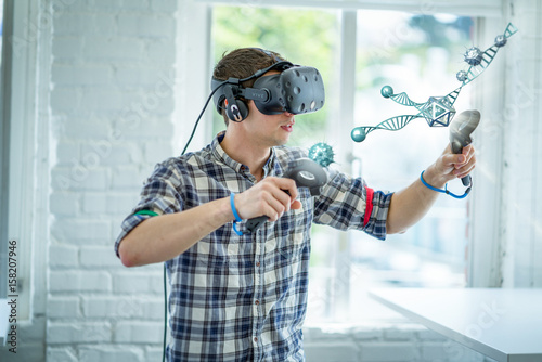 A caucasian student wearing a virtual reality headset interacts with a 3D scientific model. photo