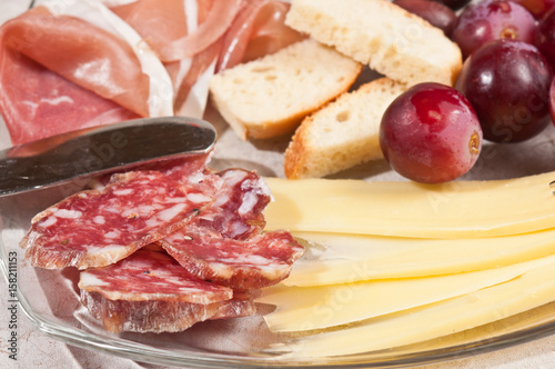 Close up ofGruyere cheese, grapes, salami, glass, red wine, cork, cheese knife, wood serving board, parings, tasty, savory healthy, lifestyle, wood bowl, brushchetta, artisan knife, italinan bread