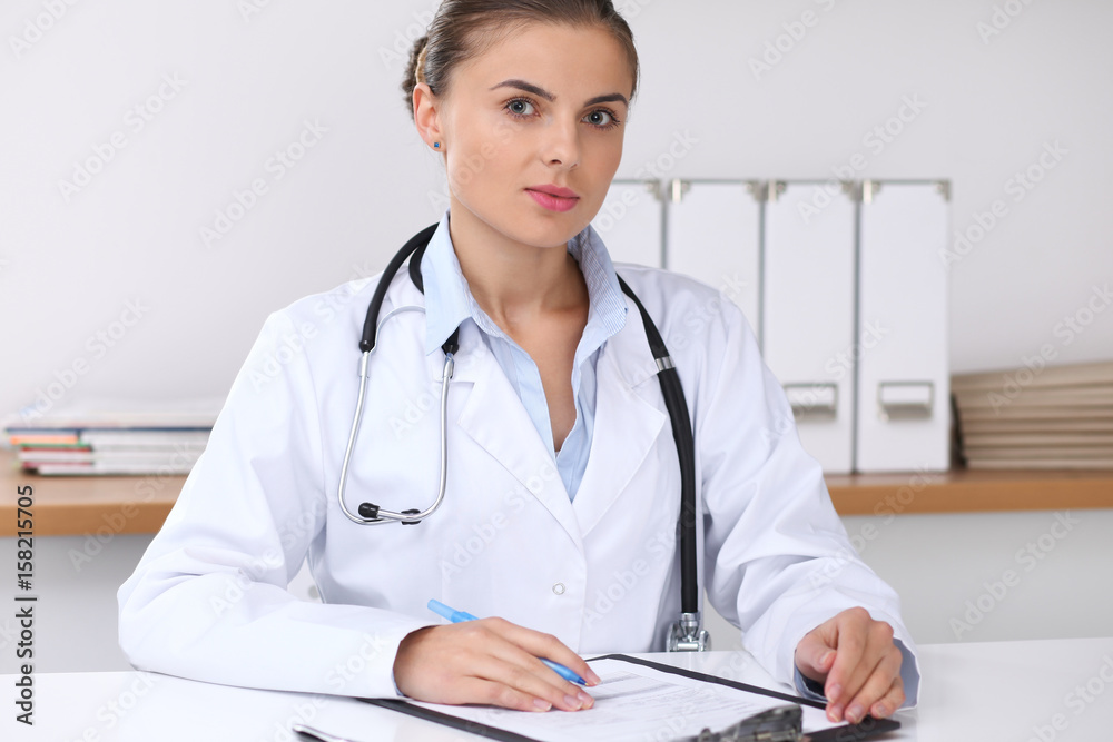 Doctor woman filling up medical form while sitting at the desk. Medicine and health care concept Doctor woman filling up medical form while sitting at the desk. Medicine and health care concept