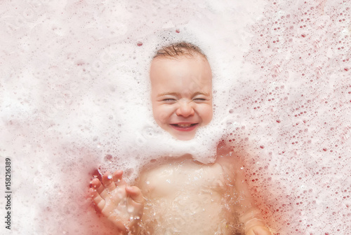 Happy baby in the bath, swimming in the foam.
