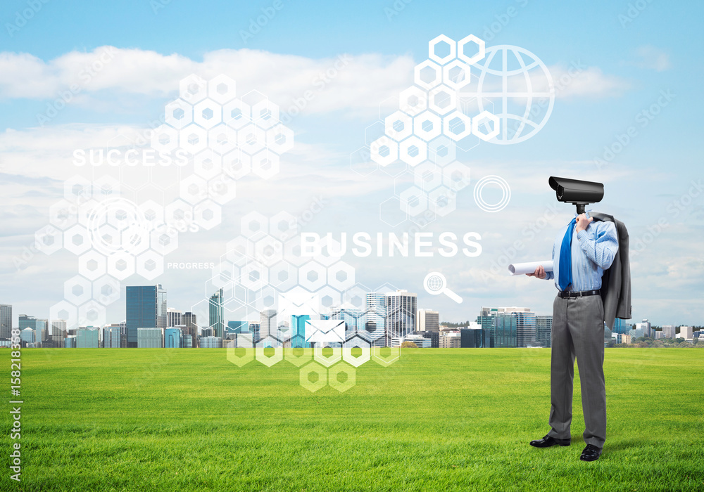 Camera headed man standing on green grass against modern cityscape Camera headed man standing on green grass against modern cityscape