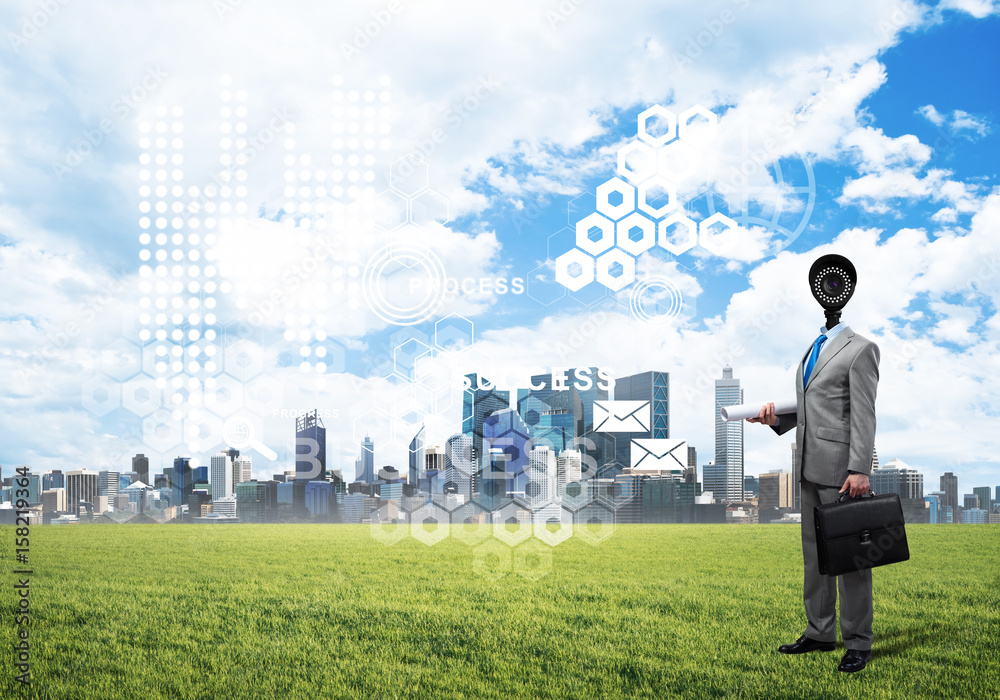 Camera headed man standing on green grass against modern cityscape Camera headed man standing on green grass against modern cityscape