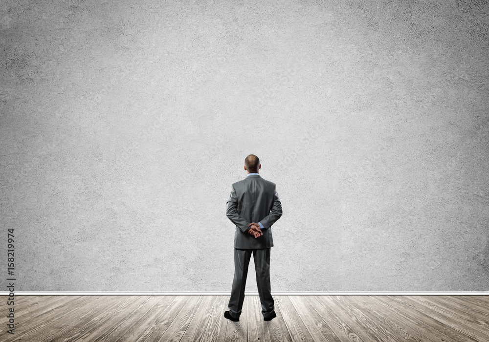 Businessman with hands behind his back and looking at blank concrete wall Businessman with hands behind his back and looking at blank concrete wall