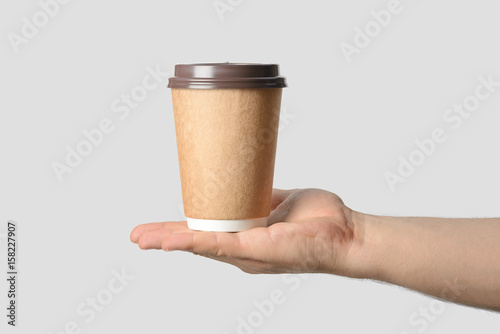 Mockup of male hand holding a Coffee paper cup isolated on light grey background.