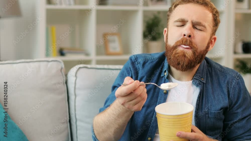 Portrait of young man who eating ice cream while relaxing on sofa in the living room at home. Portrait of young man who eating ice cream while relaxing on sofa in the living room at home.