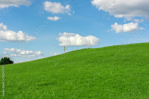 Woman in yoga position under white cloud on green field