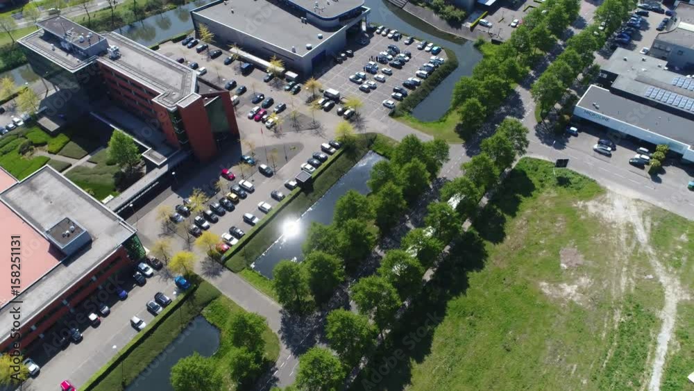 Aerial drone following car over commercial area showing two way street and several office buildings on side of street also showing small articial lakes and tree lines at side of road 4k resolution Aerial drone following car over commercial area showing two way street and several office buildings on side of street also showing small articial lakes and tree lines at side of road 4k resolution