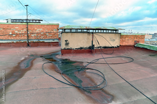 A view of the elements of the roof of a modern multi-storey brick building. Ventilation, the door to the attic, the tower elevator shaft. Wires, cables, waterproofing and drainage. St. Petersburg