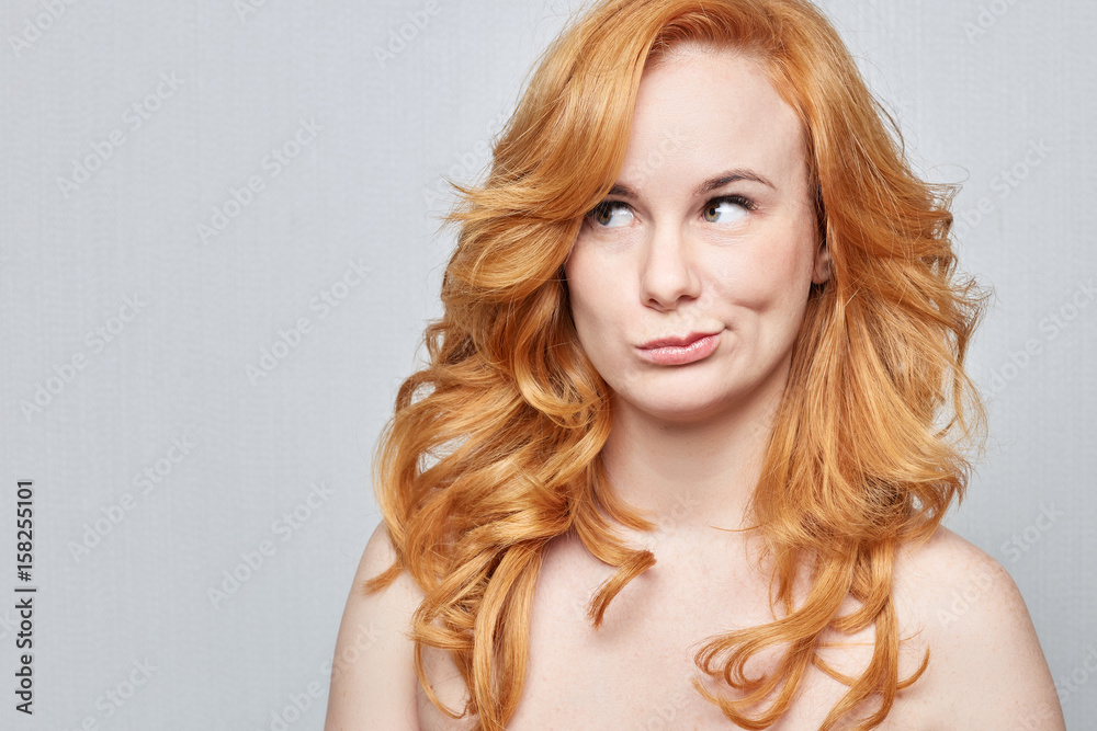 Naklejka premium I don't know.Headshot of doubtful Caucasian freckled female wearing nothing,but red long beautiful hair pouting lips and looking up with indecisive expression on her face, showing doubt and hesitation
